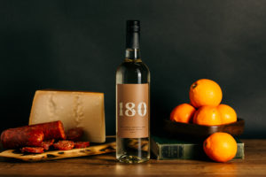 180 Estate Winery's bottle of Bourbon White wine surrounded by a block of cheese, oranges, and artisan salami